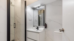 A modern bathroom with a glass shower enclosure, a white vanity with a mirror, and a toilet. - Waou Essence IV Antón Martín - Corta Duración (Madrid)