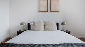 A minimalist bedroom with a large bed, two bedside lamps, and two framed abstract artworks on the wall. - Blueground | Notting Hill, w/d, nr Hyde Park (London)