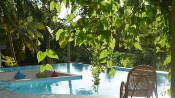 A pool area with a chair and cushions, surrounded by greenery.