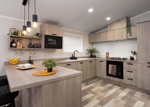 A modern kitchen with wooden cabinets, a central island, a microwave, and a gas stove. - Premium modern and contemporary luxury lodge perfect for a relaxing escape. (Workington)