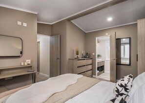 A bedroom with a bed, a dresser, a mirror, and a door leading to a bathroom. - Premium modern and contemporary luxury lodge perfect for a relaxing escape. (Workington)
