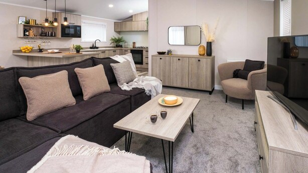 Ett modernt vardagsrum med en mörk soffa, ett ljust träbord och en tv som står på ett träskåp.