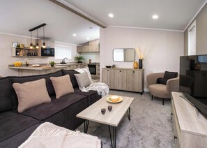 A modern living room with a dark sofa, a light wooden coffee table, and a TV on a wooden cabinet. - Premium modern and contemporary luxury lodge perfect for a relaxing escape. (Workington)