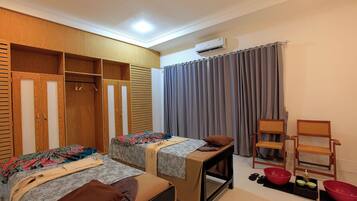 A room with two beds, a wooden wardrobe, a table with a chair, and a large red bowl.