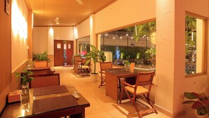 Un vestíbulo de hotel con zona de comedor, ventiladores de techo, plantas en macetas y vistas al exterior.
