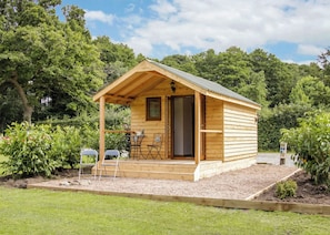 A small wooden cabin with a porch, a table, and chairs.