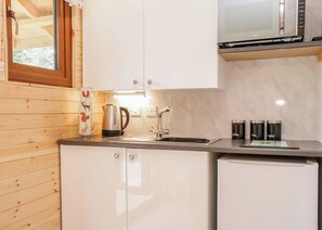 A compact kitchen with wooden walls, a stainless steel kettle, a coffee maker, and a microwave.