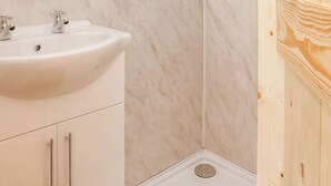 A bathroom with a white sink, two faucets, and a wooden panel on the wall. - 1 bedroom accommodation in Oswestry (Oswestry)