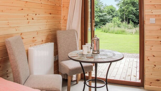 A wooden cabin room with a table, chairs, and a view of a green landscape. - 1 bedroom accommodation in Oswestry (Oswestry)