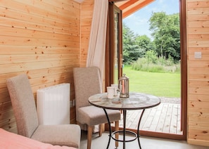 A wooden cabin room with a table, chairs, and a view of a green landscape.