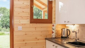 A wooden cabin with a kitchen area, including a sink, stove, and a window with a view of greenery. - 1 bedroom accommodation in Oswestry (Oswestry)