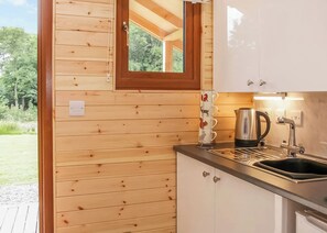 A wooden cabin with a kitchen area, including a sink, stove, and a window with a view of greenery.