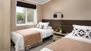A bedroom with two beds, a window with a view, a bedside table with a lamp, and a wall-mounted light.