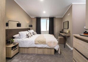 A modern bedroom with a bed, bedside tables, a desk, a mirror, and a window.