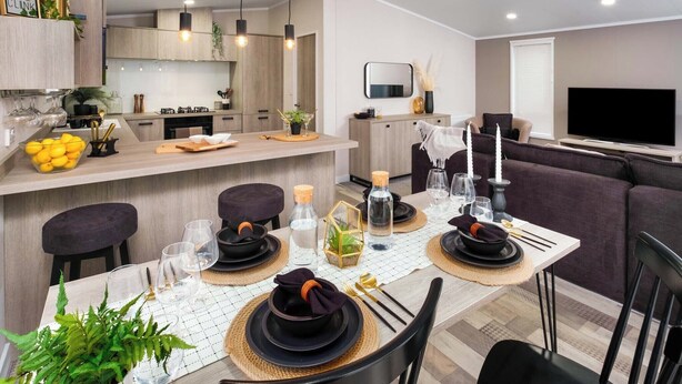 A modern kitchen with pendant lighting, a dining area set for a meal, and a living room with a flat-screen TV.
