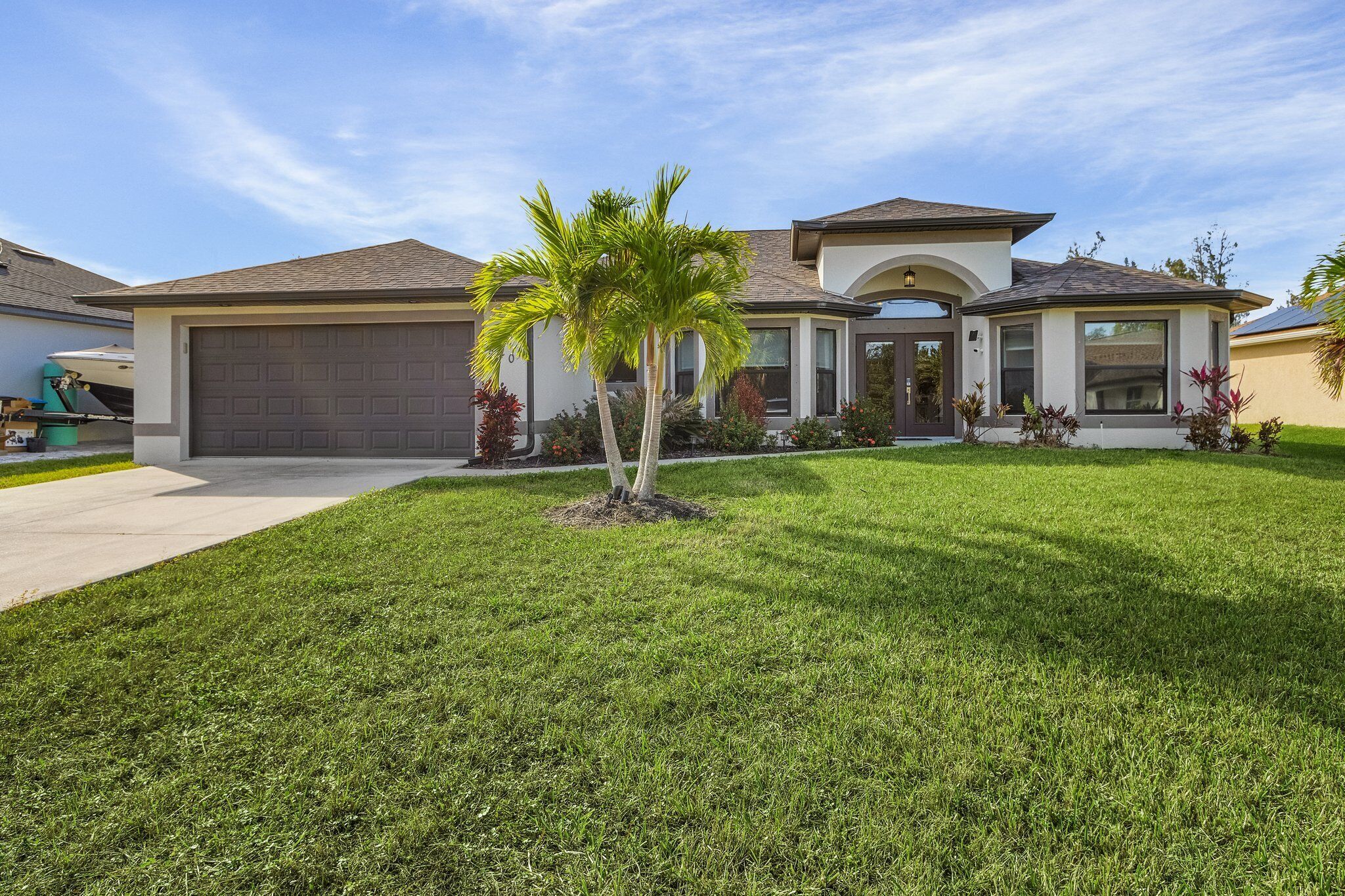 A modern two-story house with a garage, a well-maintained lawn, and a palm tree.