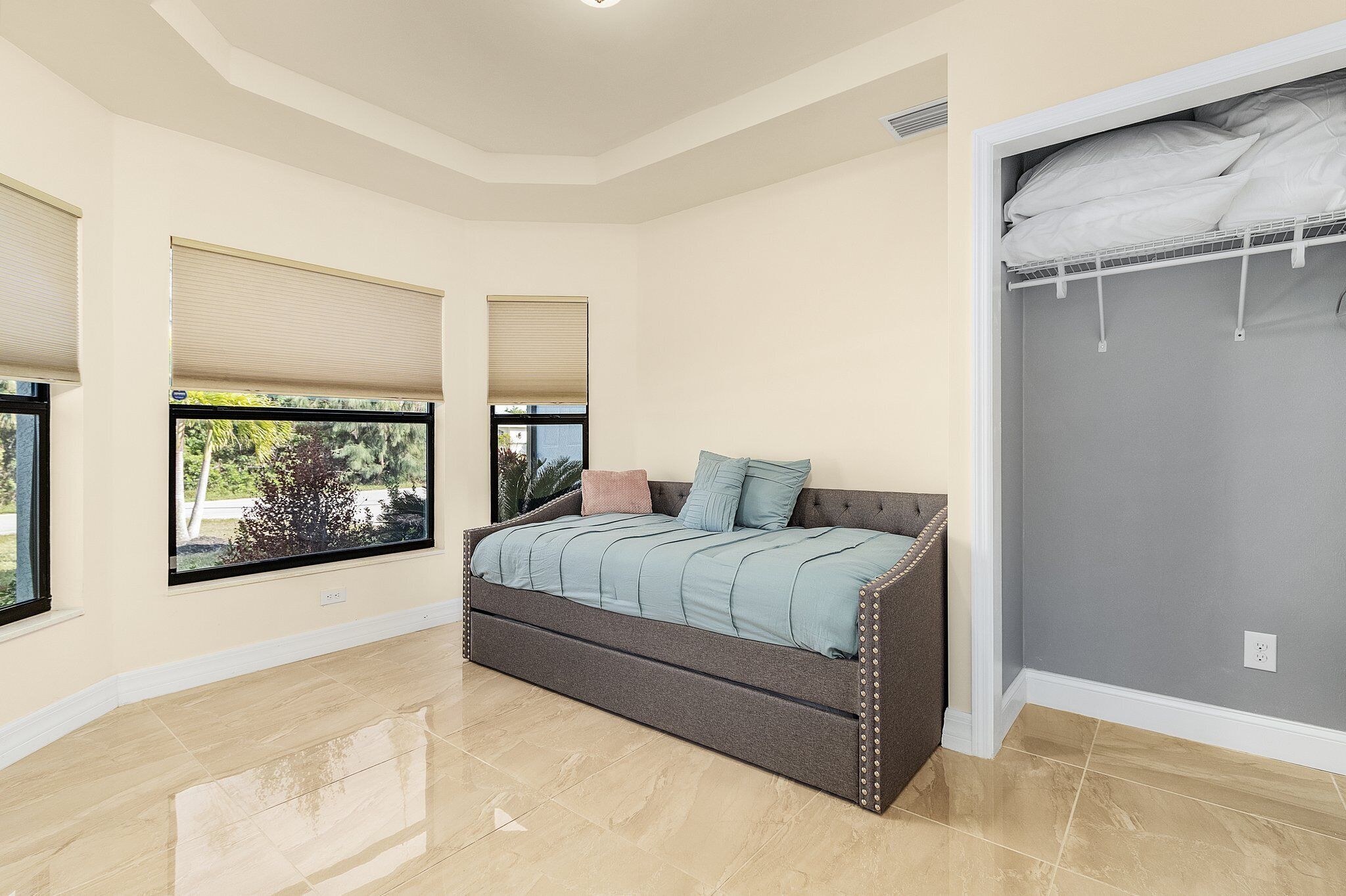 A bedroom with a bed, large windows, a closet, and a tiled floor.