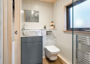 A compact bathroom with a marble sink, a toilet, a mirror, and a window. - Meadowsweet Treehouse (Ellesmere)