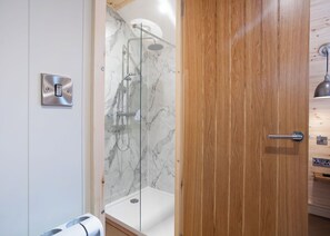 A modern bathroom with a glass-enclosed shower, marble walls, and a wooden door.
