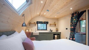 Ein Schlafzimmer mit Bett, Fenster, Küchenzeile inklusive Spüle und Schränken sowie Blick ins Freie.