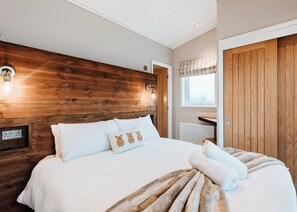 A bedroom with a wooden headboard, a bed with white bedding, a bedside table with a lamp, and a window with blinds. - 2 bedroom accommodation in Bridgnorth (Bridgnorth)