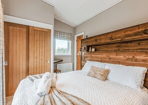A bedroom with a wooden headboard, a large bed with white bedding, a window with blinds, and a wooden wardrobe. - 2 bedroom accommodation in Bridgnorth (Bridgnorth)