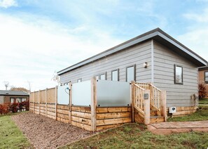 A modern single-story building with a grey exterior, a wooden fence, and a small staircase leading to a door marked with the number 2. - 2 bedroom accommodation in Bridgnorth (Bridgnorth)