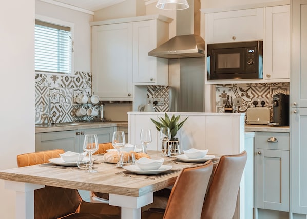A modern kitchen with white cabinets, a stainless steel range hood, a microwave, and a dining area with a wooden table set for a meal.