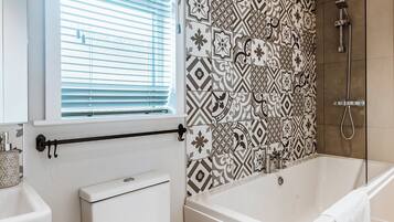 A bathroom with a bathtub, a toilet, a window with blinds, and a shower area.