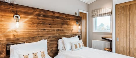A bedroom with two beds, wooden headboard, wall-mounted lights, a window with blinds, and a radiator.