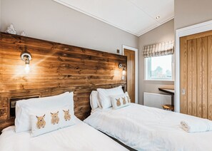 A bedroom with two beds, wooden headboard, wall-mounted lights, a window with blinds, and a radiator. - 2 bedroom accommodation in Bridgnorth (Bridgnorth)
