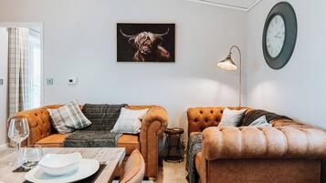 A modern living room with two brown leather sofas, a dining table with a white plate and glass, and a large clock on the wall.