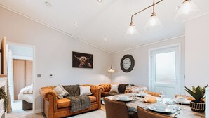 Un salon moderne comprenant un canapé, une table à manger et des chaises, une horloge et une fenêtre donnant sur un beau paysage.