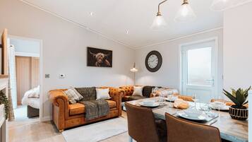 A modern living room with a sofa, dining table, and chairs, a clock, and a window with a view.