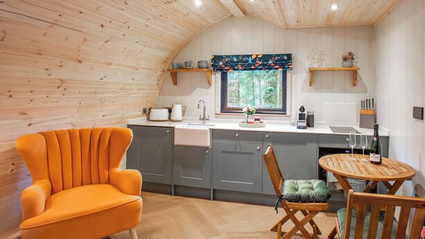 Una cocina acogedora con techo de madera, armarios grises, una mesa de comedor de madera y una silla naranja.