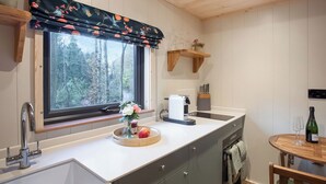 Una cocina con ventana, estanterías de madera, un lavamanos, una cafetera y un comedor con mesa y sillas.