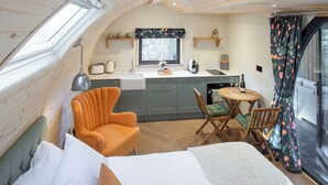 Una habitación acogedora con una cama, una silla, una mesita, un ventanal y una kitchenette.