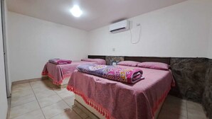 A room with two beds, each covered with pink blankets and a patterned quilt. There is an air conditioning unit on the wall. - La Regional (Loreto)