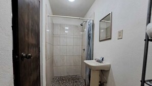 A small bathroom with a shower, a sink, and a mirror. - La Regional (Loreto)