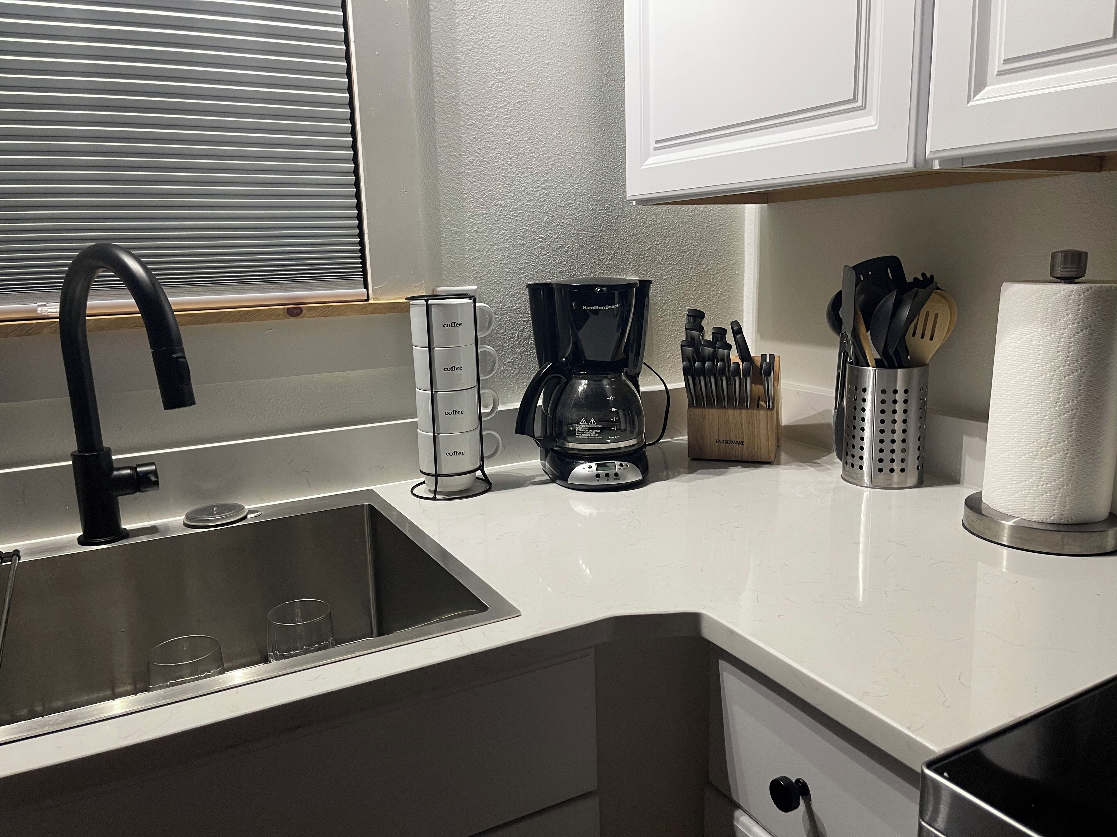 A kitchen with a sink, coffee maker, and utensils.