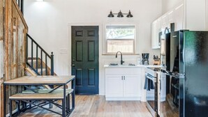 A kitchen with white cabinets, a black refrigerator, and a wooden staircase.