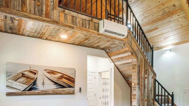 A cozy living room with a grey sofa, checkered cushions, a wooden staircase, and a painting of boats on the wall.