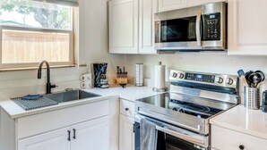 A modern kitchen with white cabinetry, a stainless steel stove, a microwave, and a sink with a faucet.