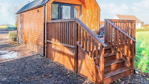 A wooden cabin with a curved roof, a wooden staircase, and a small deck area.