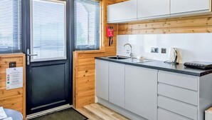 A modern kitchen with a black door, wooden walls, a stainless steel sink, and a black countertop.
