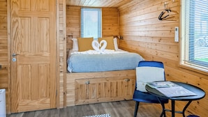 A compact wooden cabin room with a bed, a small table, a chair, and a wardrobe.