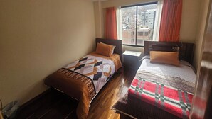 Una stanza con due letti, una finestra con tende e vista sugli edifici.
