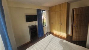 Una camera da letto con un letto, una televisione a parete, armadi in legno e una finestra con tende.