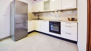 A modern kitchen with white cabinets, a stainless steel refrigerator, a built-in oven, and a wooden ceiling. - Apartment Lada by Interhome (Omiš)