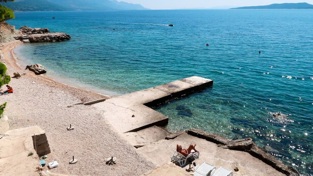 A beach with clear water, a pier, and rocky terrain. - Apartment Lada by Interhome (Omiš)